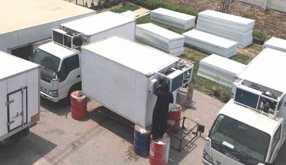 Refrigerated truck bodies being fitted to Isuzu chassis beside stacked PIR panel stock in the Izhar Foster yard